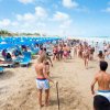 Spiaggia affollata con lettini blu e numerosi bagnanti.