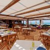 Un ristorante all'aperto con tavoli apparecchiati, vista mare e pergolato in legno.