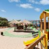 Area giochi su sabbia con scivoli e ombrelloni in paglia.