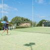 Partita di tennis in corso su un campo all'aperto, con spettatori sullo sfondo.