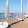 Spiaggia affollata con barche a vela sulla sabbia e persone che camminano.