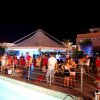 Festa notturna all'aperto vicino a una piscina con persone che socializzano sotto una tenda.