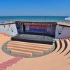 Anfiteatro all'aperto vuoto con vista sul mare, gradinate circolari e palco centrale.