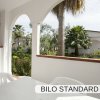 Veranda con tavolo bianco di plastica, archi aperti su vista di palme e giardino.