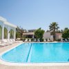 Piscina rettangolare con sdraio bianche e edificio bianco con tende verdi.