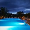 Piscina illuminata di sera, circondata da lettini e palme.