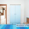 Bilocale standard con letto blu, armadio azzurro e cucina in lontananza.