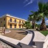 Edificio giallo con palme e vialetto pavimentato sotto un cielo blu.