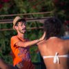Uomo con cappello e occhiali, in maglietta arancione, guida attività all'aperto.