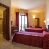 Camera d'hotel con due letti singoli, copriletto rosso e una porta a vetro aperta su un balcone.