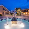 Fontana illuminata con statua e getti d'acqua, circondata da edifici.