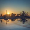 Piscina al tramonto con palme e sedie a sdraio riflesse nell'acqua.