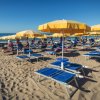 Spiaggia soleggiata con lettini blu e ombrelloni gialli allineati.