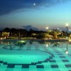 Piscina illuminata di notte con palme e cielo crepuscolare.