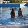Due donne parlano in una piscina con lettini sullo sfondo.