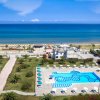 Una piscina con ombrelloni e lettini vicino a una spiaggia sabbiosa e mare calmo.
