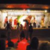 Band che suona su un palco con luci colorate e persone che ballano.
