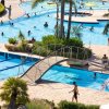 Piscina con ponticello, palme e persone che nuotano e prendono il sole.