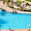 Piscina azzurra con ombrelloni, sdraio e persone che si rilassano.