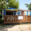 Una casa mobile con veranda in legno, tettoia blu e gialla e circondata da alberi.